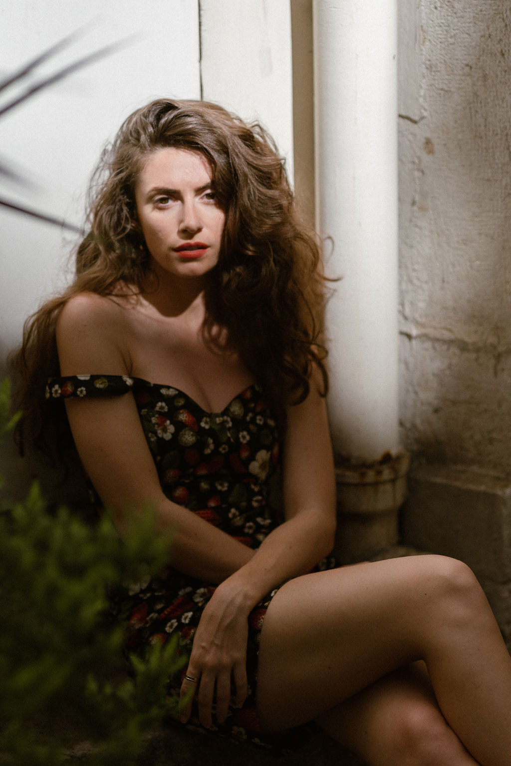 Smiling woman with long wavy brown hair resting her face on her hand against a plain light background.
