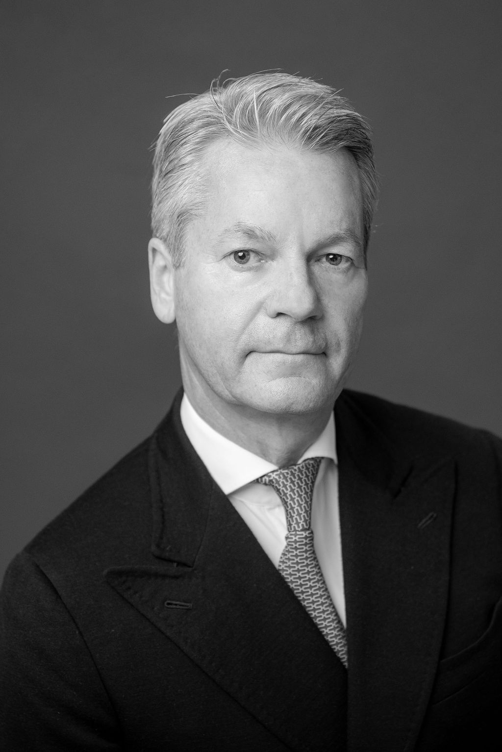 Black and white portrait of a middle-aged man with gray hair wearing a suit and patterned tie against a plain background.